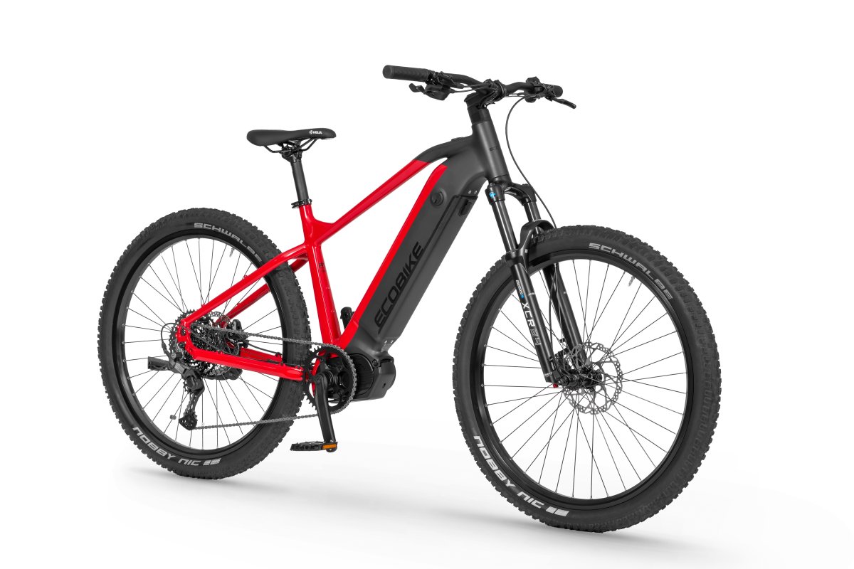 Widok elektrycznego roweru górskiego — rama w matowej czerni i jaskrawej czerwieni, koła z grubymi oponami terenowymi, widoczny akumulator zamontowany w dolnej rurze ramy i amortyzator przedni.