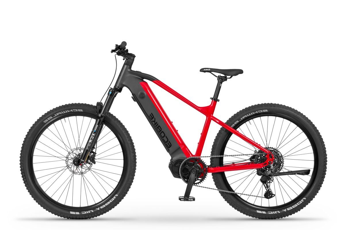 Profilowe ujęcie elektrycznego roweru górskiego — rama w matowej czerni i jaskrawej czerwieni, koła z grubymi oponami terenowymi, widoczny akumulator zamontowany w dolnej rurze ramy i amortyzator przedni.